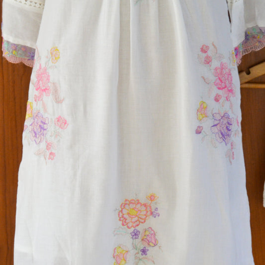 White garment with colorful floral embroidery on a wooden hanger.