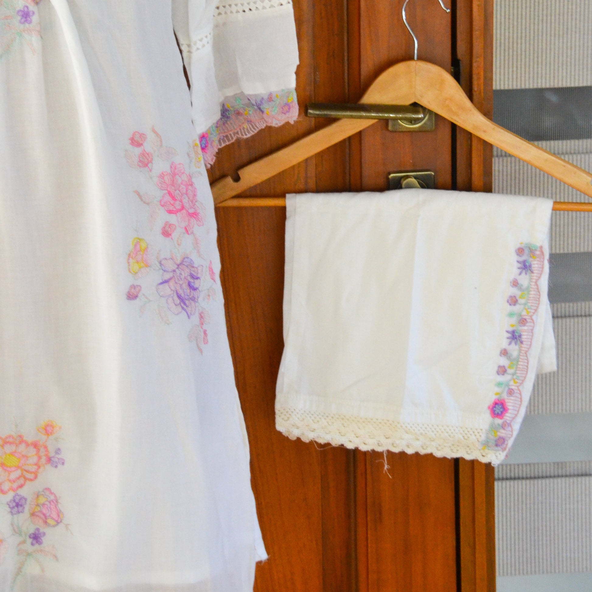 White embroidered garment on a wooden hanger against a wooden door.